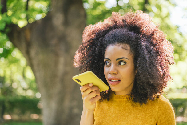 Hezká afro žena posílá audio zprávu na svém mobilu. - Fotografie, Obrázek