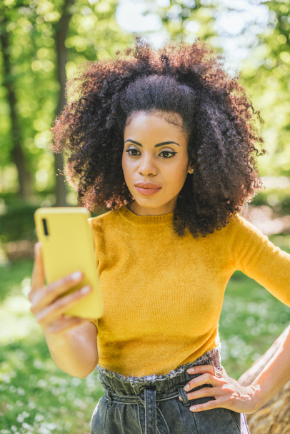 Mulher afro bonita olhando para celular, em um jardim. - Foto, Imagem
