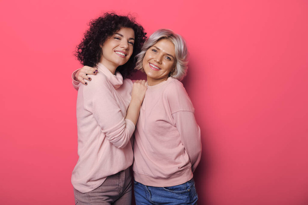 Monocromo foto de hermanas caucásicas sonriendo a la cámara abrazándose en una pared rosa - Foto, imagen