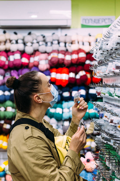 Женщина в маске для лица выбирает изделия из бусин в магазине ремесел. Концепция магазинов - Фото, изображение