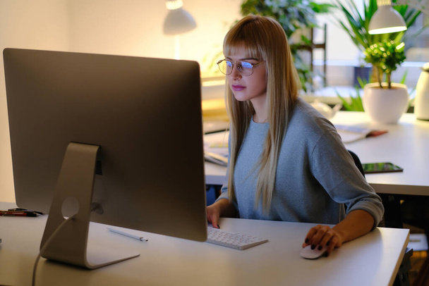 Quarto de escritório acolhedor e mulher bonita usando um computador à noite - Foto, Imagem