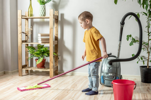 Un niño está limpiando el suelo de una habitación usando una fregona. Concepto de independencia, ayuda a los padres, tareas domésticas del niño - Foto, imagen