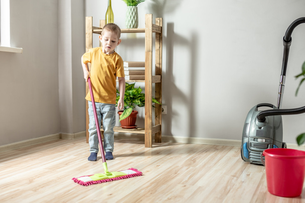 Mały chłopiec sprząta podłogę w pokoju mopem. Pojęcie niezależności, pomoc rodzicom, prace domowe dziecka - Zdjęcie, obraz