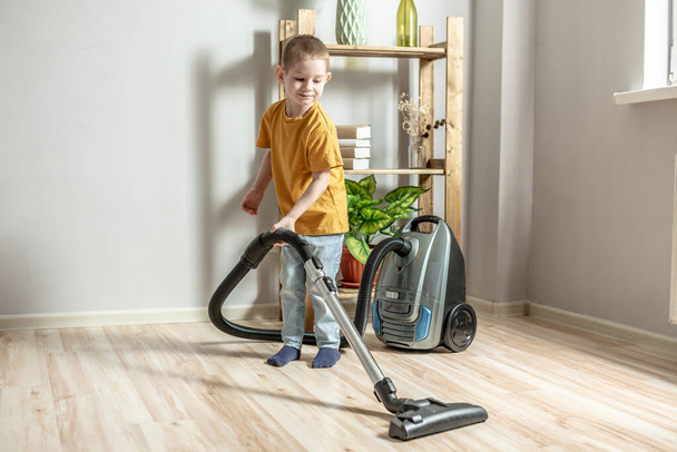 Un niño pequeño ayuda a sus padres en las tareas domésticas, limpiando el piso con una aspiradora - Foto, imagen