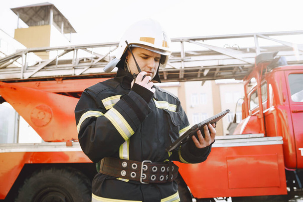 Male firefighter with tablet in uniform on car background - Valokuva, kuva