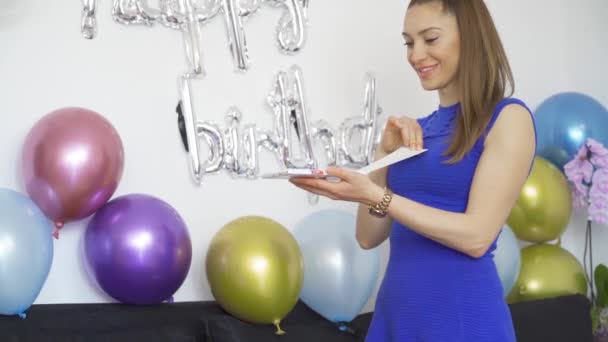 Έκπληκτη Νεαρή γυναίκα ανοίγει ένα δώρο γενεθλίων στο πάρτι γενεθλίων με πολύχρωμα μπαλόνια - Πλάνα, βίντεο