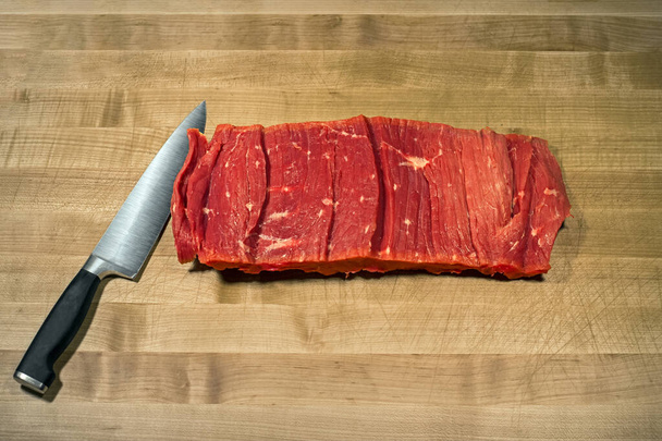 Čerstvé červené filety ze syrového hovězího masa s ostrým lesklým řeznickým nožem z nerezové oceli na dřevěném podstavci stolu. Horní pohled plochý, volné místo pro text - Fotografie, Obrázek