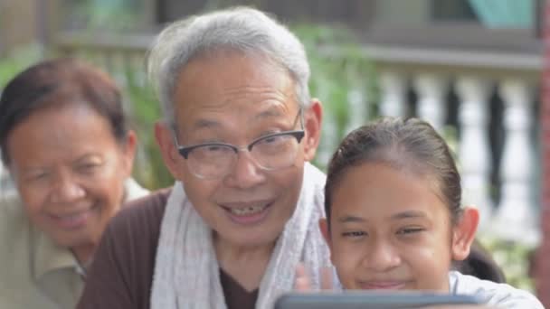 Ázsiai imádnivaló lány és idős nagyszülei élvezik, hogy kommunikálni az emberekkel segítségével videohívás mobil okostelefon tartózkodása alatt otthon. A családi kötelék. Szelektív fókusz. - Felvétel, videó