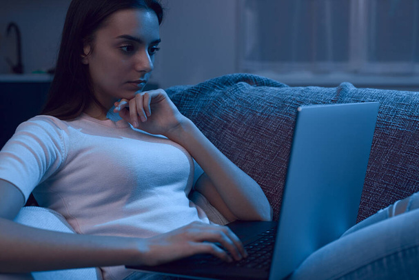Młoda kobieta korzystająca wieczorem z laptopa na kanapie - Zdjęcie, obraz