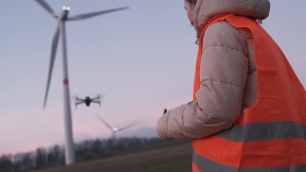 Engenheira usa um drone para verificar o desempenho do sistema de turbina selvagem ou moinho de vento ao pôr do sol. - Filmagem, Vídeo