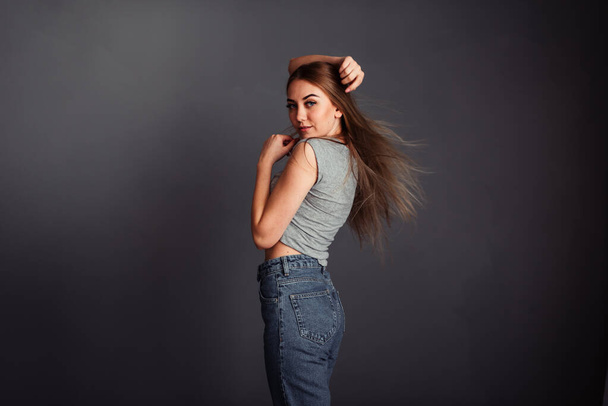 Blond-haired girl dancing with raised hands up on a plain gray t-shirt and jeans on a gray background. - Fotoğraf, Görsel