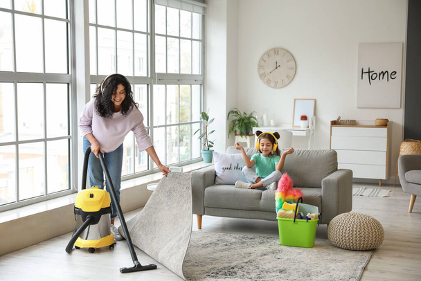 Mother and daughter listening to music while hoovering floor in flat - Photo, Image