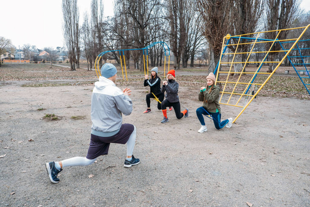 Gruppen-Fitnesstraining im Freien. Sozial entfernte Outdoor-Workouts in öffentlichen Parks. Drei Frauen und ein Mann trainieren gemeinsam im öffentlichen Park. Gesundheits-, Wellness- und Gemeinschaftskonzept - Foto, Bild