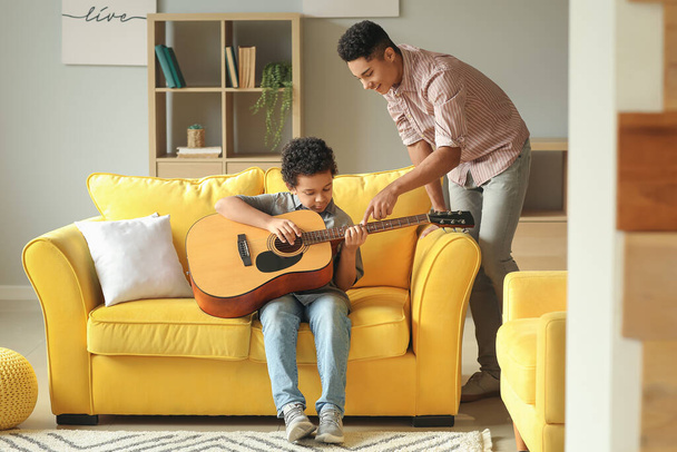 Έφηβος μαθαίνει στον μικρό του αδερφό να παίζει κιθάρα στο σπίτι. - Φωτογραφία, εικόνα