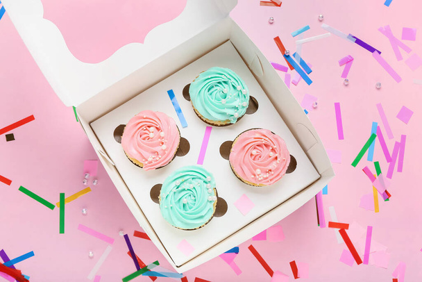 Doboz ízletes cupcakes és konfetti színes háttér - Fotó, kép