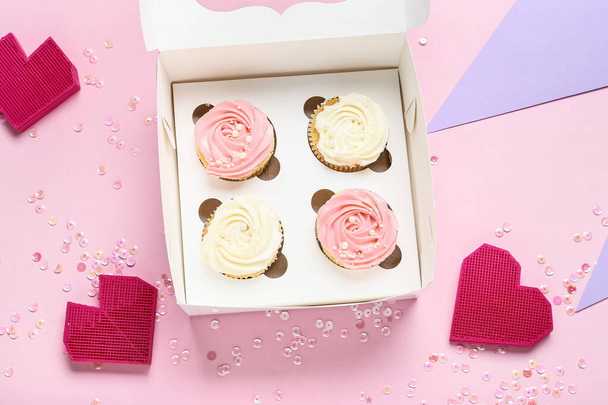 Schachtel mit leckeren Cupcakes und Dekor auf farbigem Hintergrund - Foto, Bild