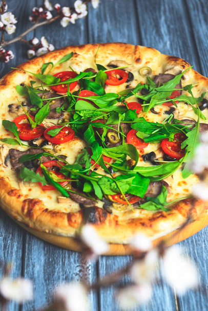 Rustic tasty pizza with meat, mushrooms, tomatoes and basil. Over wooden table, photo in dark tones. Italian cuisine concept, fast food, junk food. - Foto, imagen
