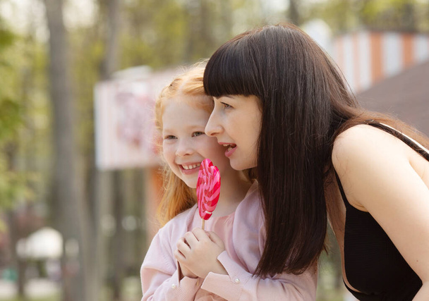 Young beautiful mother and her adorable red hair daughter in a summer park. - Foto, imagen