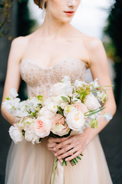 Νύφη σε ένα όμορφο φόρεμα κρατά ένα μπουκέτο λουλούδια στα χέρια της - Φωτογραφία, εικόνα