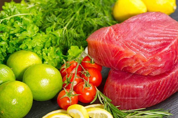 Tonnikalan raakaa pihviä, tonnikalan sashimia, tonnikalaa viipaloituna vihanneksilla. terveellistä syömistä äyriäisten kanssa, kokkaamme kotona. kalanliha layout mustalla kivellä - Valokuva, kuva