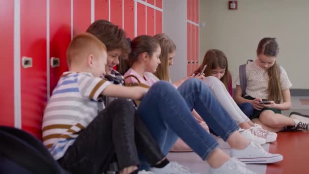 Seguimiento de vídeo de los escolares utilizando el teléfono inteligente en el pasillo cerca de taquillas. Fotografía con cámara de helio RED en 8K. - Imágenes, Vídeo