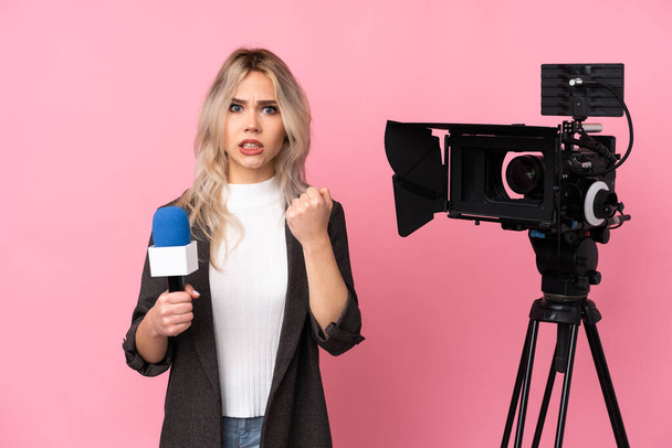 Reporter kobieta trzyma mikrofon i raportuje wiadomości na odizolowanym różowym tle sfrustrowany złą sytuacją - Zdjęcie, obraz