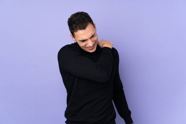 Young caucasian handsome man with turtleneck sweater isolated on purple background suffering from pain in shoulder for having made an effort - Photo, Image