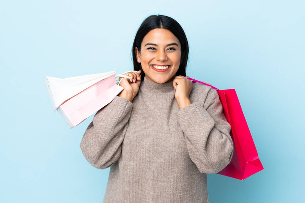 Giovane donna latina isolata su sfondo blu con borse della spesa e sorridente - Foto, immagini