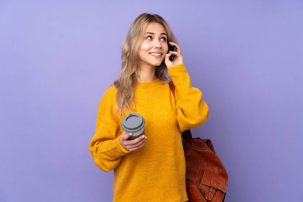 Teenager russische Studentin isoliert auf lila Hintergrund hält Kaffee zum Mitnehmen und ein Handy - Foto, Bild