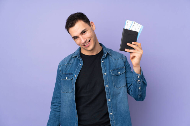 Young caucasian handsome man isolated on purple background happy in vacation with passport and plane tickets - Foto, immagini