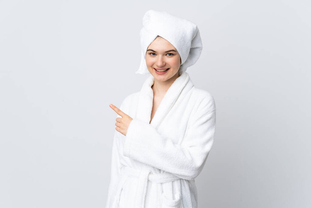Teenager girl in a bathrobe isolated on white background pointing to the side to present a product - Foto, Imagem