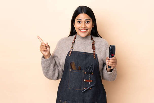 Young Colombian woman hairdresser isolated on beige background pointing finger to the side - Photo, Image
