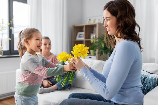 daughters giving daffodil flowers to happy mother - Фото, зображення