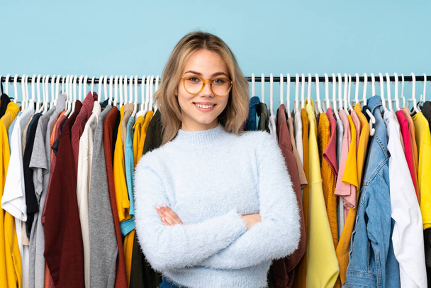 Teenager Russian girl buying some clothes isolated on blue background with glasses and smiling - Foto, afbeelding