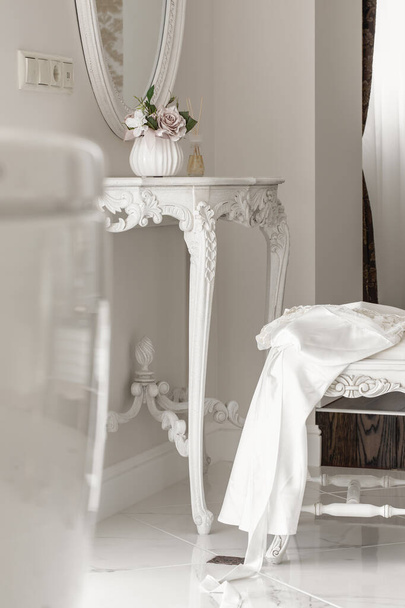 Vestido de seda blanco en silla cerca de la consola blanca en el interior de la hermosa luz. Concepto de boda - Foto, imagen