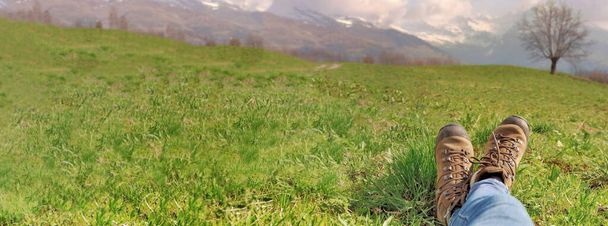 panorámás kilátás a lábát egy nő farmerben, és visel túracipő feküdt a fűben az alpesi réten  - Fotó, kép
