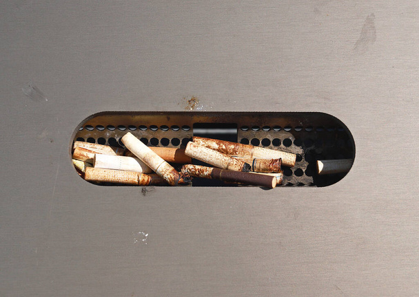 Rabos de cigarro em uma lixeira de metal em uma parada de ônibus. Cinzeiro de rua com pontas de cigarro. Caixa de areia de aço inoxidável, com cinzeiro. Conceito de maus hábitos. - Foto, Imagem