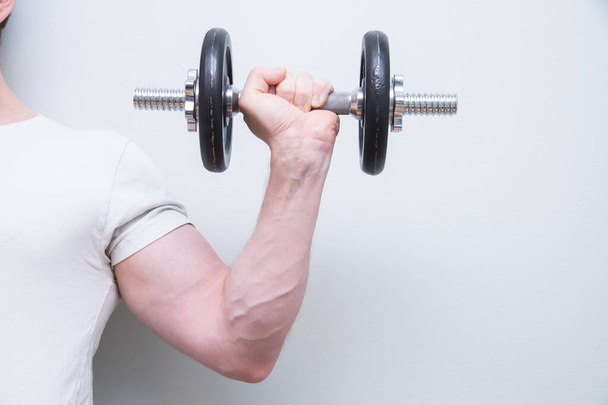 An athletic male working out with a dumbbell against a white wall - Photo, Image
