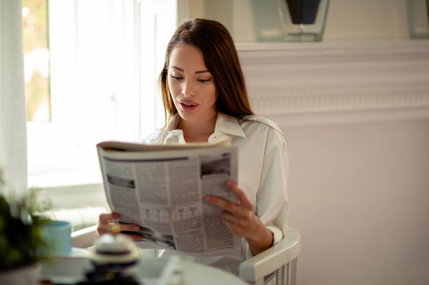 Portrait of young woman reading the news while having coffee in her kitchen - Foto, immagini