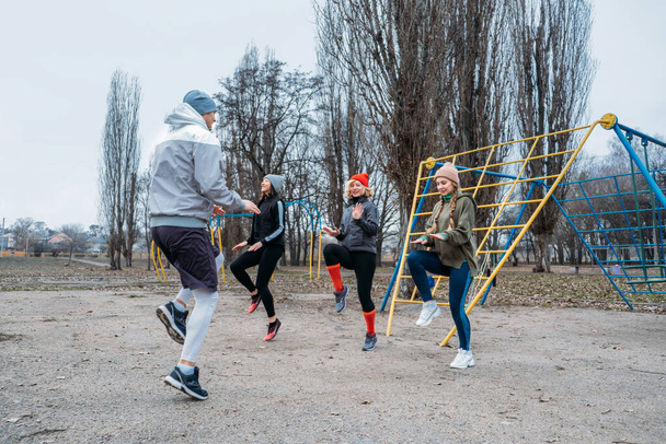 Group fitness workout classes outdoors. Socially Distant Outdoor Workout Classes in public parks. Three women and man training together in the public park. Health, wellness and community concept - Zdjęcie, obraz