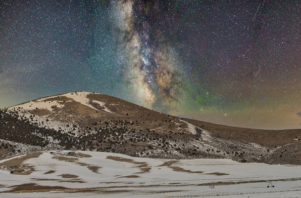 Blick auf eine winterliche Hügellandschaft und Milchstraße am nächtlichen Sternenhimmel - Foto, Bild