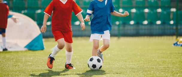 草の上でサッカーをしているスポーツの赤と青のジャージーシャツの幸せな子供たち。学校の子供のためのスポーツサッカー教育 - 写真・画像