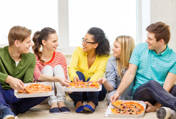 five smiling teenagers eating pizza at home - Фото, изображение