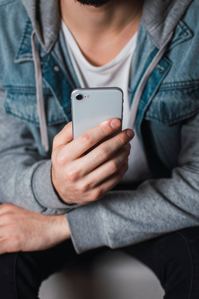 A vertical shot of a sitting guy scrolling through his smartphone - Foto, Bild