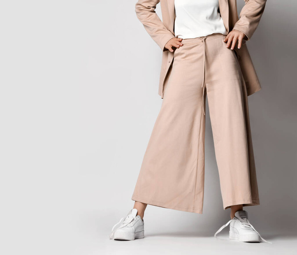 Legs of woman in beige business smart casual suit and sneakers standing over light. Stylish business female wear - Фото, зображення