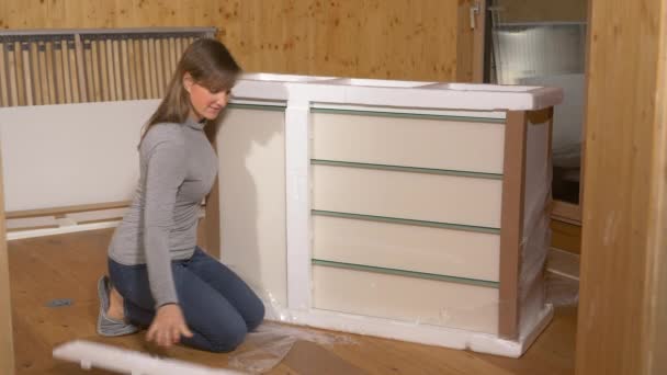 Sluiten: Jonge vrouw pakt een nieuwe ladekast uit tijdens het inrichten van de slaapkamer. - Video
