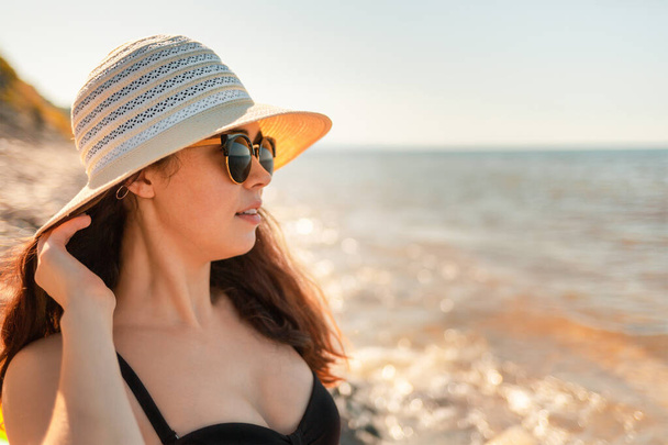 Eine junge attraktive Frau mit Hut und Sonnenbrille blickt in die Ferne. Das Meer im Hintergrund. Tönung und Nahaufnahme. - Foto, Bild