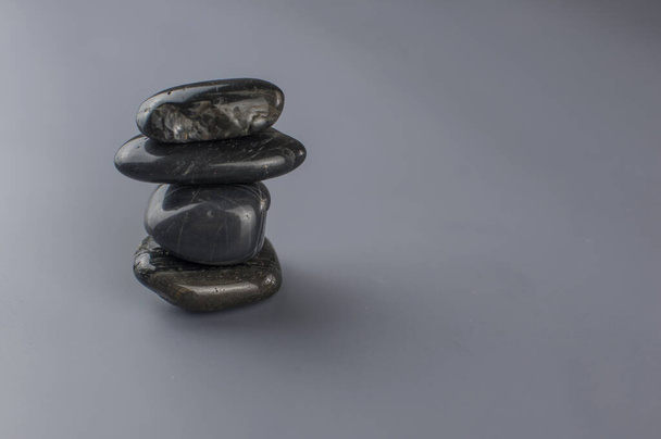 Чорні камені для масажу, складені на сірому паперовому фоні, група гальки у вежі, гармонія і баланс
.  - Фото, зображення