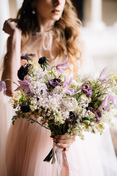 Bruid in een mooie roze jurk houdt een boeket wilde bloemen in haar handen - Foto, afbeelding