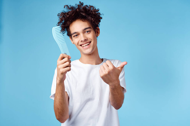 emotional man with a comb in his hand and curly hair in a blue background Copy Space - Photo, Image